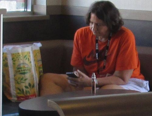 Man and woman who always illegally smoke their electronic cigarettes at McDonald's or McDonalds - Mc Donald's or Mc Donalds  - Woman sitting down at the table she always sits at with her electronic cigarette 